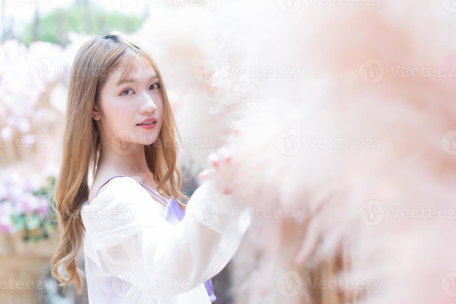 Asian beautiful woman with long bronze hair who wears short skirt and white long sleeve stands in the colorful garden. photo