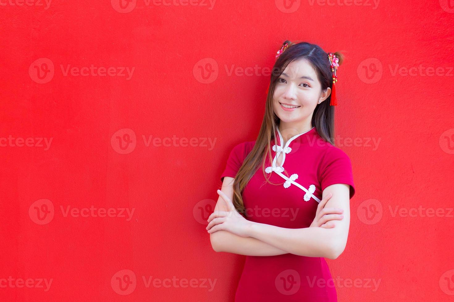 Beautiful Asian woman wears a red cheongsam and arm crossed while looks at to camera and smiles happily with the red background. photo