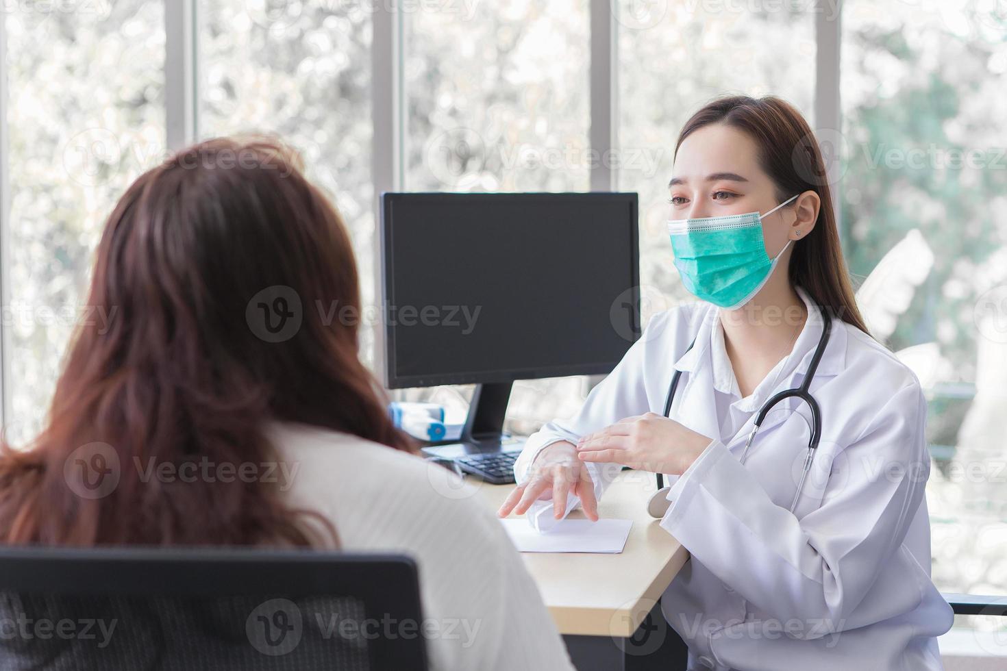 Asian elderly woman patient is checked health by professional doctor while both wear medical face mask at the examination room in hospital. photo