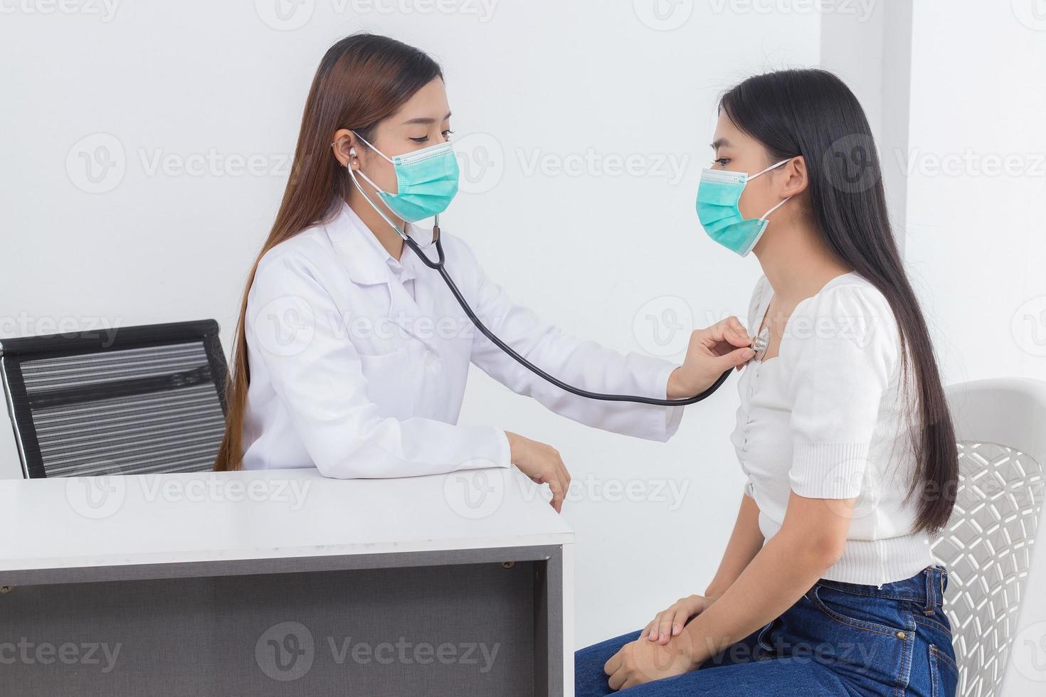 Asian female doctor examines symptom of her patient while both wear medical face mask to prevent infection disease COVID 19 in hospital. photo