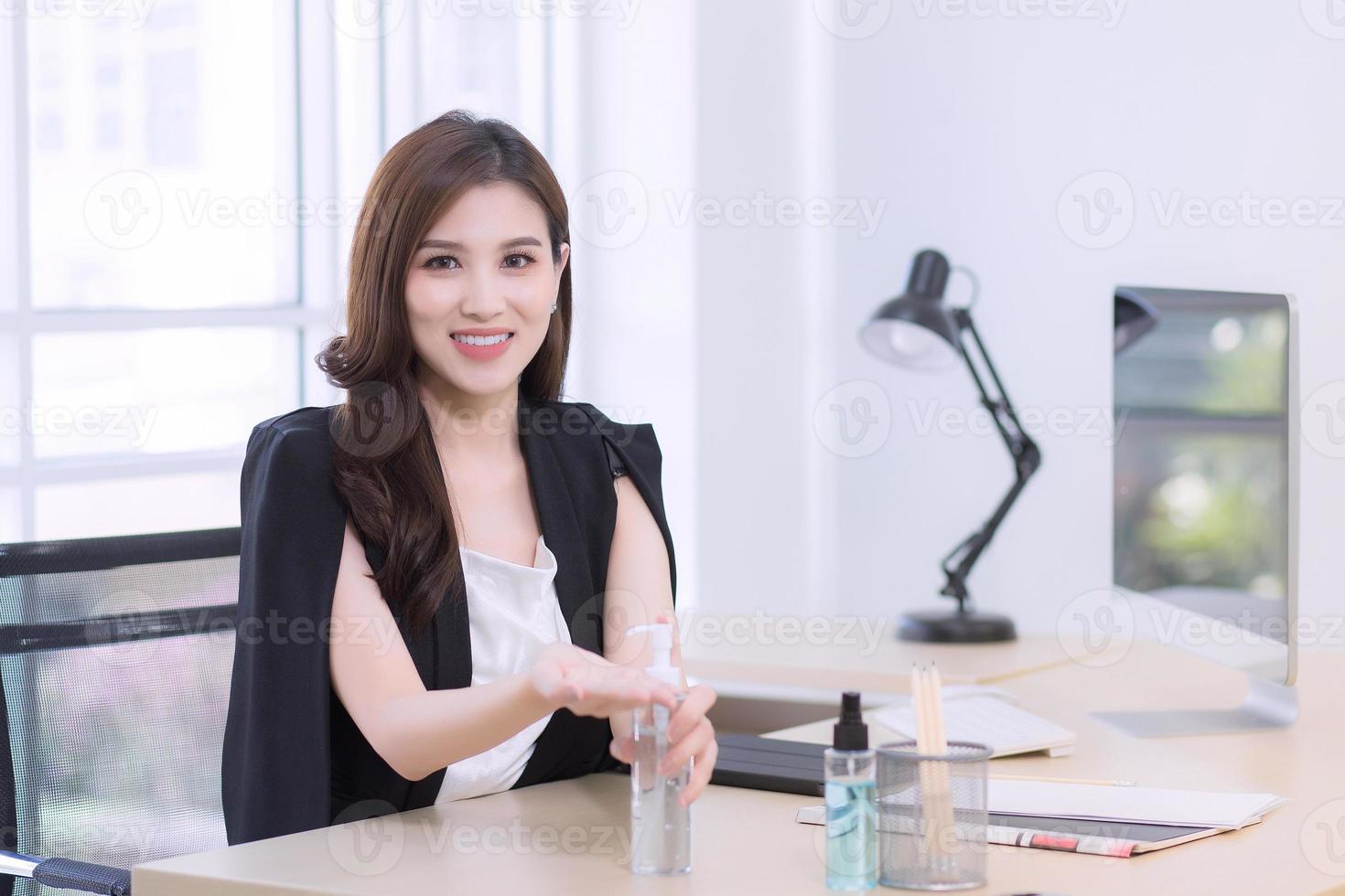 A beautiful office woman is sitting and pressing an alcohol gel. photo