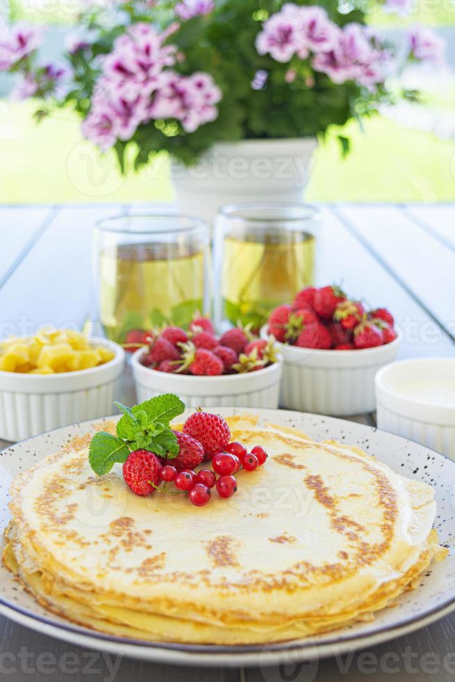 Pancakes with caramelized apples, raspberries, strawberries and red currants. Brunch with green tea and crepes. photo