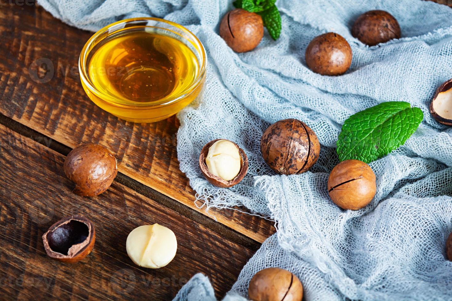 Macadamia nuts in shell with mint leaves and honey on wooden background photo