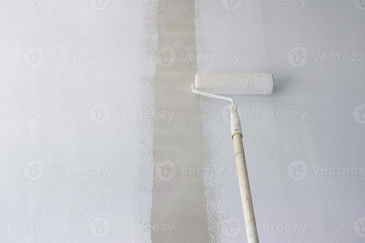 Long handle roller brush applying primer white paint on cement wall background, buildind and home renovation concept photo