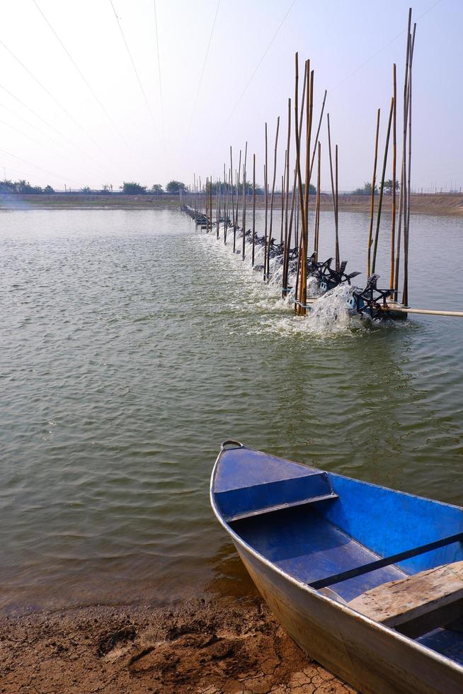 Selective focus at part of blue boat with aerator multiple turbine wheels on water surface and nylon lines structure over shrimp pond for prevents birds from interfering in natural shrimp farm photo