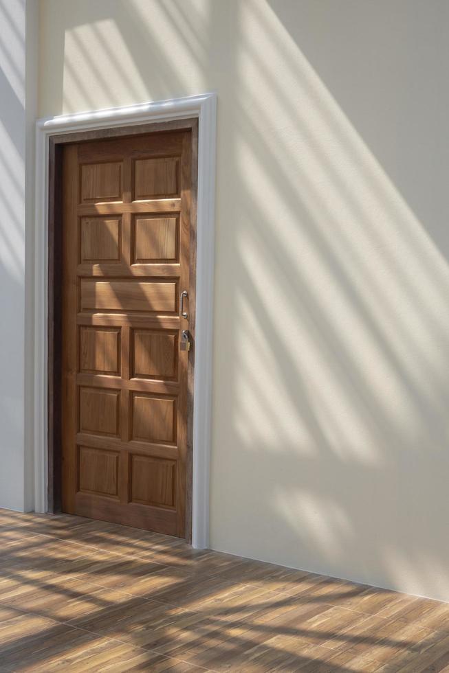 Side view of wooden door in mastic color cement wall with sunlight and shadow of roof structure on wood floor tiles surface inside of house building site in vertical frame photo