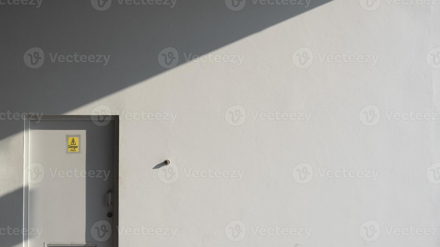 Sunlight and shadow on surface of gray wall and door of electrical control room with yellow warning sign in minimal style, exterior architecture concept photo