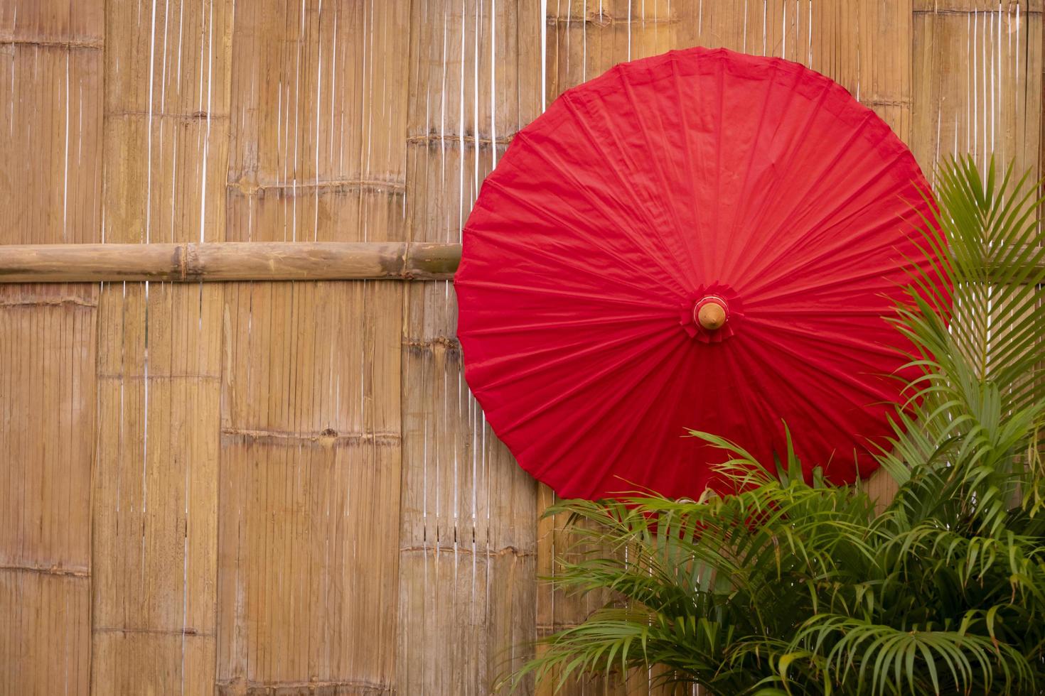 Red paper umbrella with green palm leaves on bamboo wooden wall background,  wall decoration design concept photo