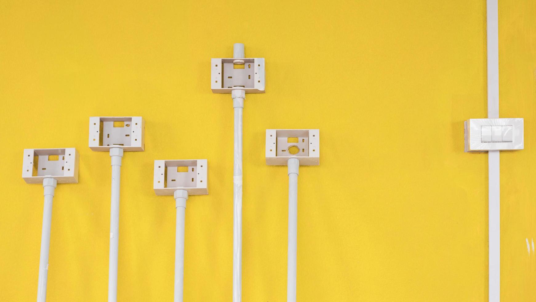 White plastic light switch box with pipe line and electric socket boxes on yellow cement wall background inside of house construction site photo