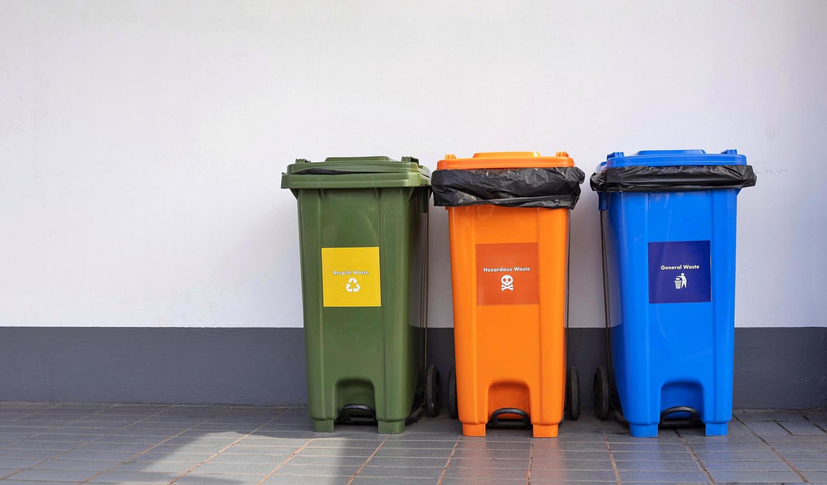 tres cubos de basura multicolores en el suelo de baldosas y fondo de pared de cemento en la zona pública foto