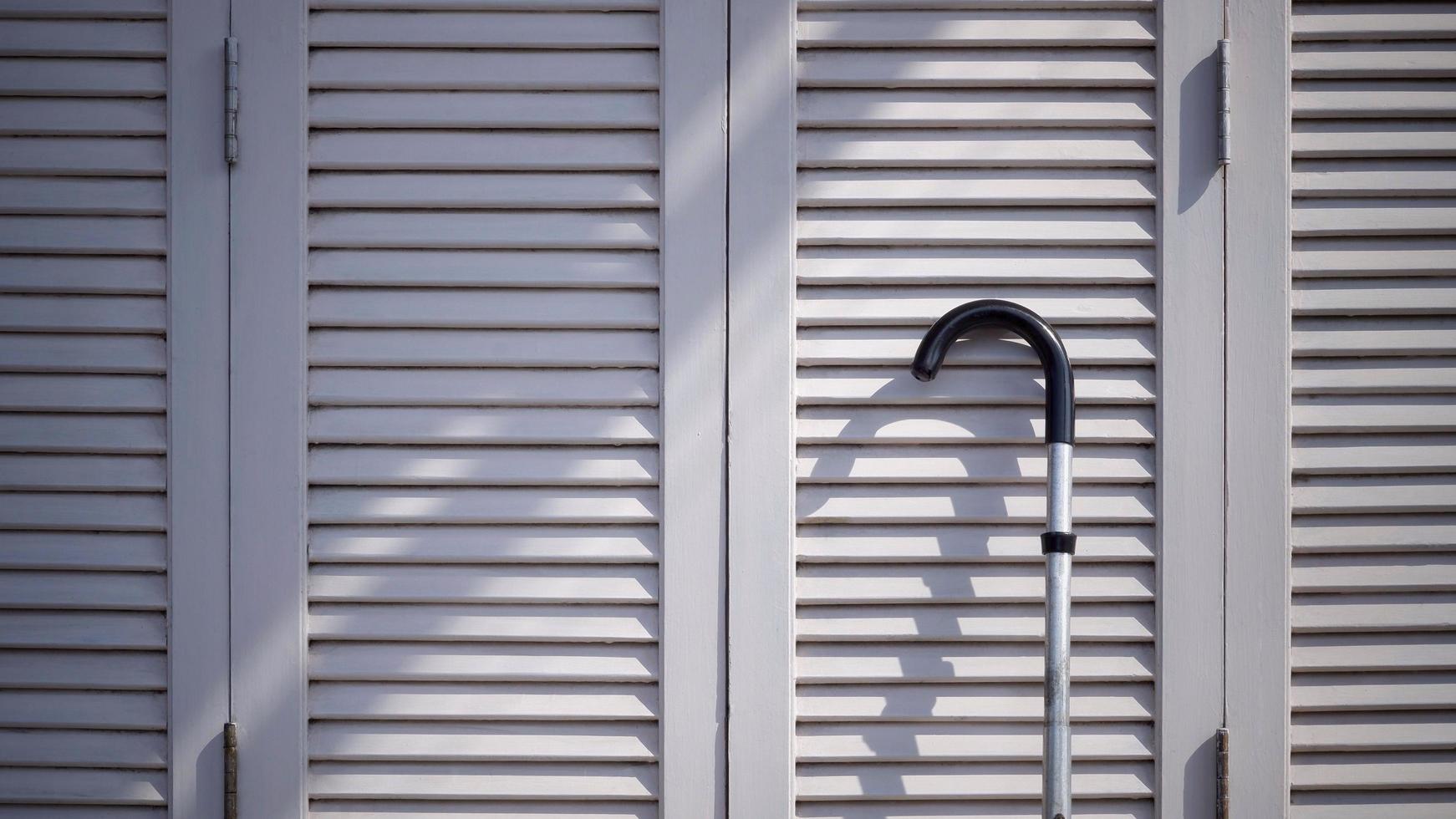 Sunlight and shadow on surface of the old metal walking stick on white wooden folding wall background photo