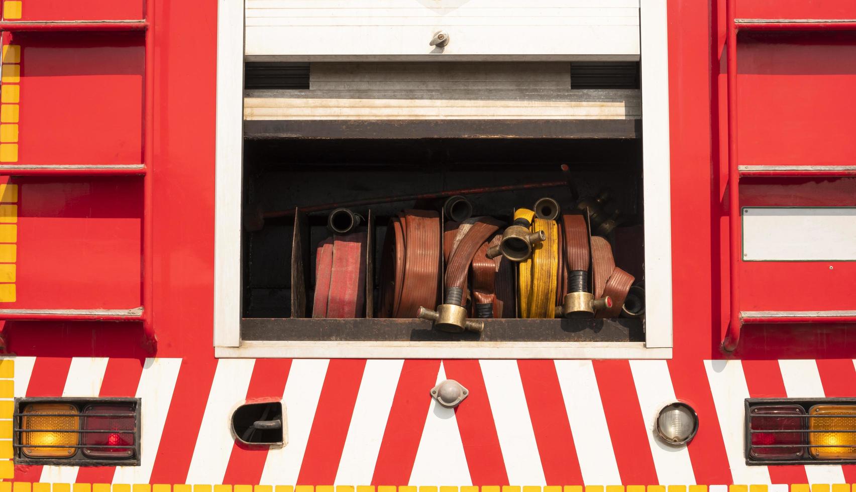 Compartment of the old rolled up fire hoses, stairs, taillights, hook with red and white stripes on rear side view of fire truck photo