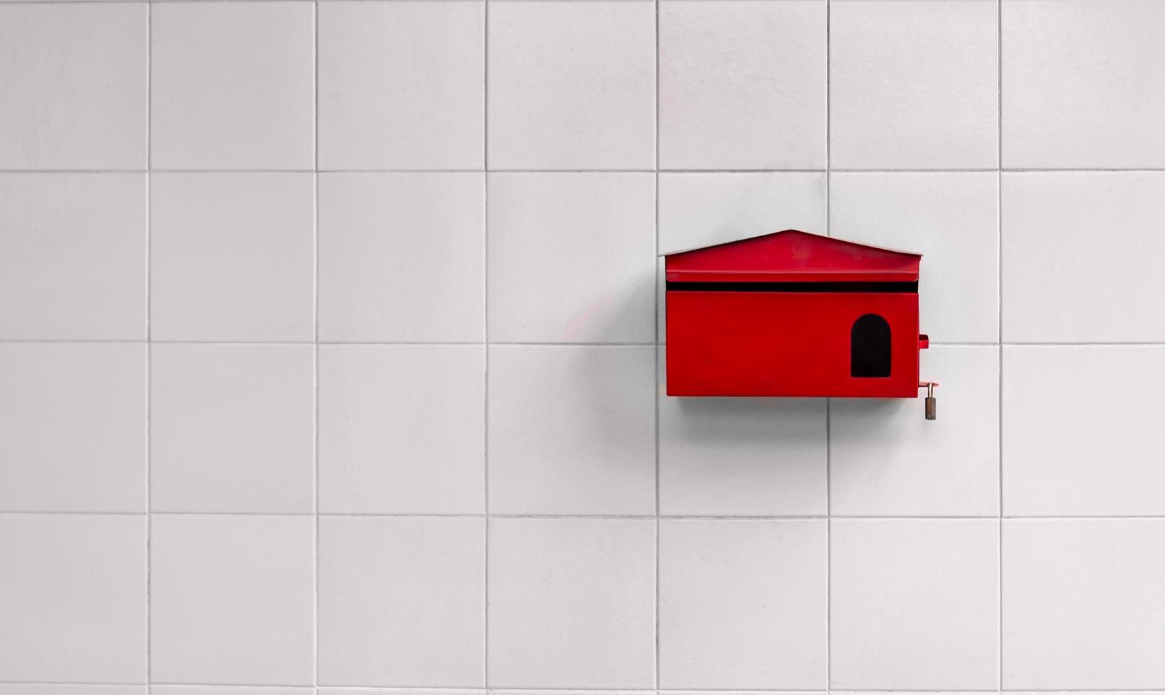 Red mailbox hanging on white tiles wall background photo