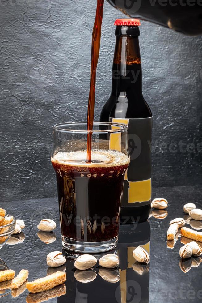 Glasses with different types of craft beer on a wooden bar. In glasses and bottles. Nuts and crackers on the table. On a dark background. photo