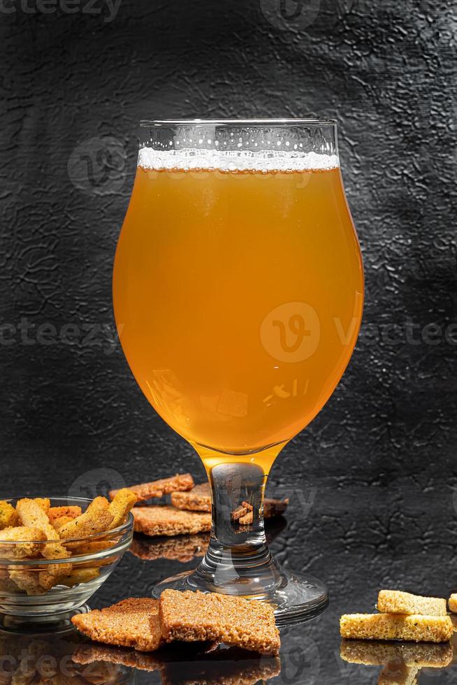 Glasses with different types of craft beer on a wooden bar. In glasses and bottles. Nuts and crackers on the table. On a dark background. photo