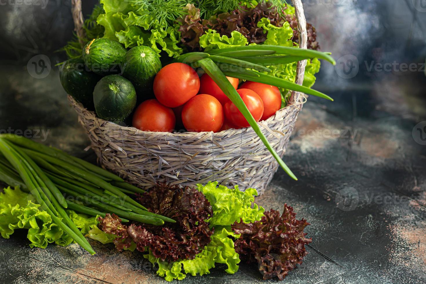 Fresh vegetables for salad in a basket. Tomatoes and cucumbers with zucchini and cabbage with dill. Spring harvest, benefits and vitamins. On a dark background. photo