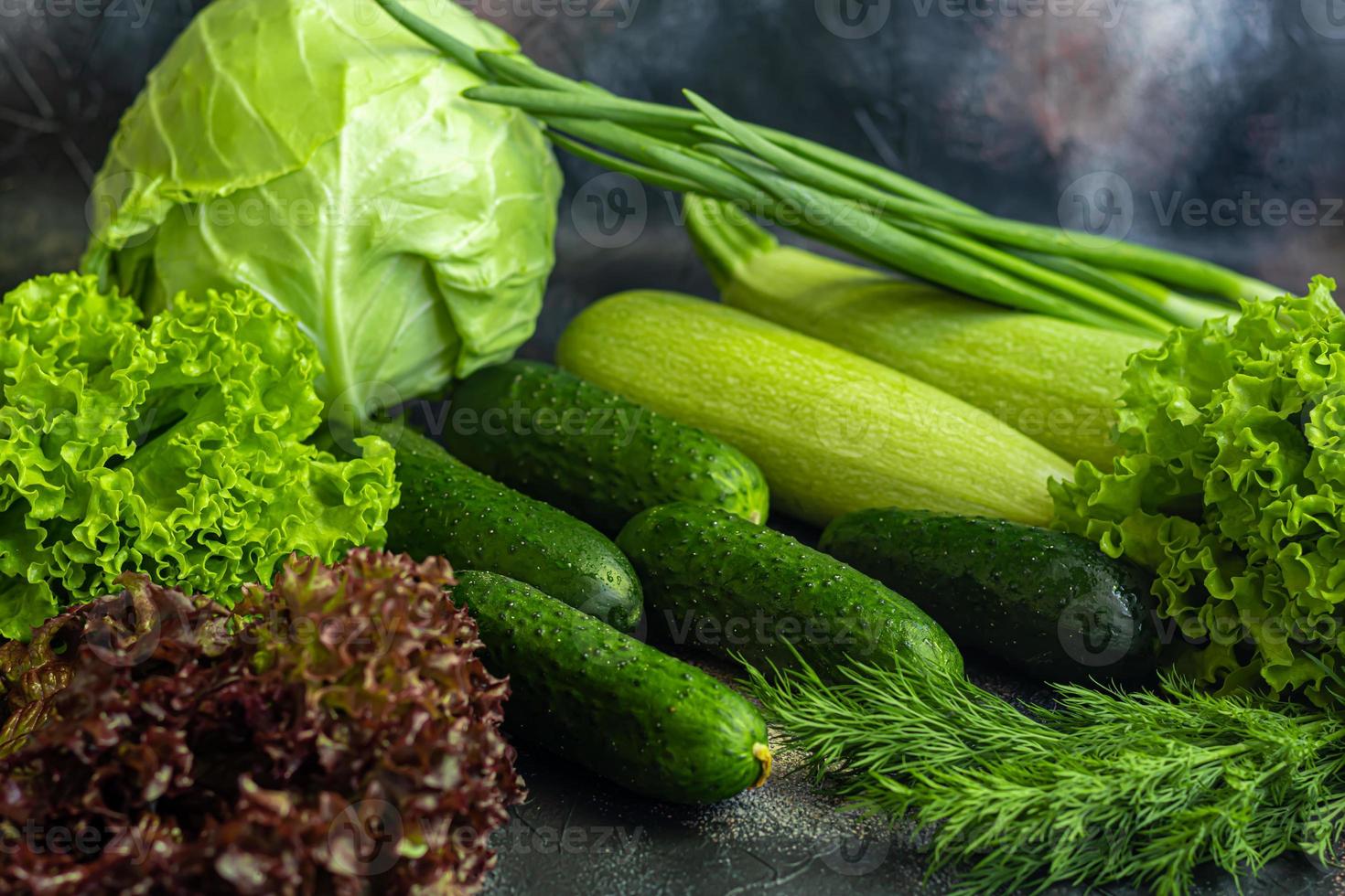 Fresh vegetables for salad. Tomatoes and lettuce, cucumbers with zucchini and cabbage with dill. Spring harvest, benefits and vitamins. On a dark background. photo
