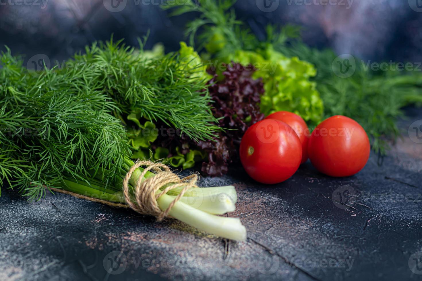 Fresh vegetables for salad. Tomatoes and lettuce, cucumbers with zucchini and cabbage with dill. Spring harvest, benefits and vitamins. On a dark background. photo