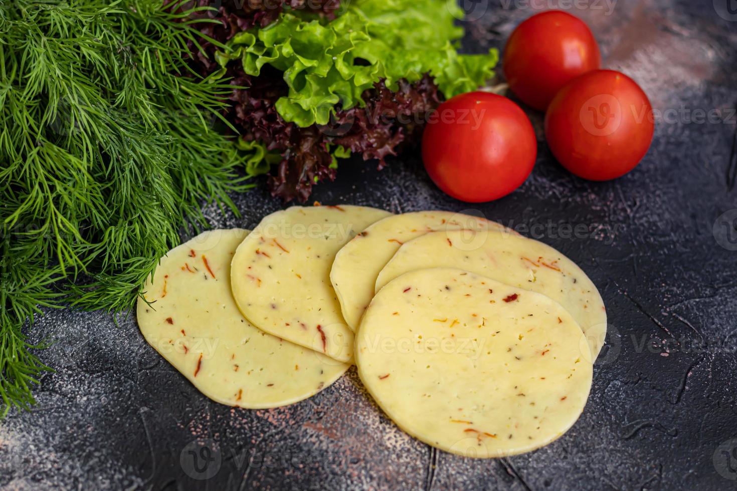 Sliced cheese with slices of tomatoes and bell peppers. Along with spring vegetables. On a dark background. photo