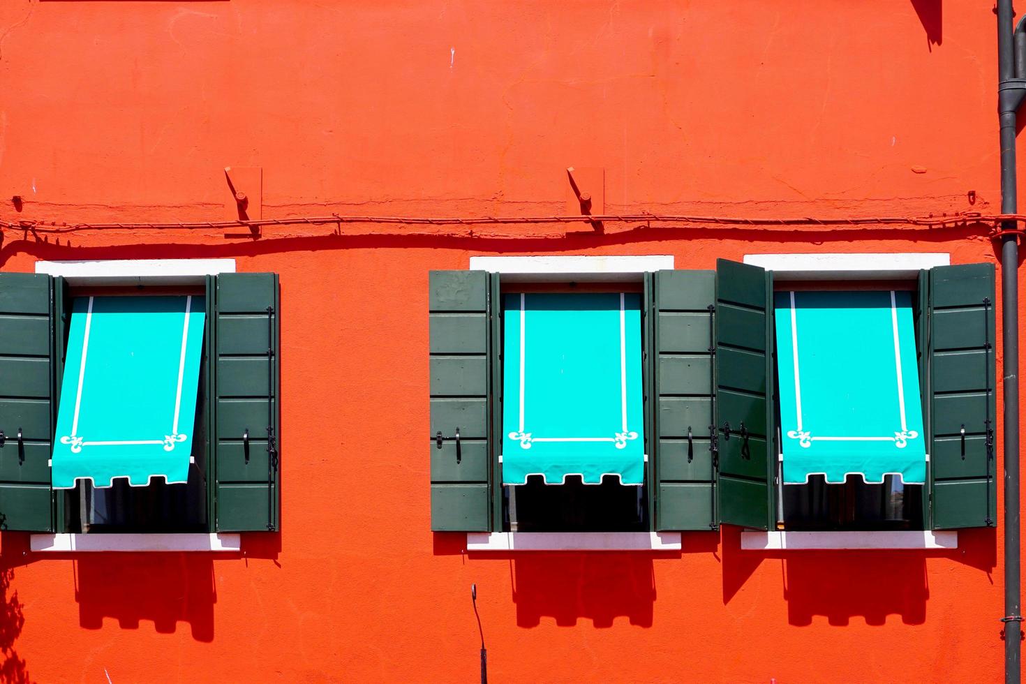 tres ventanas con dosel azul en burano en la pared naranja roja foto