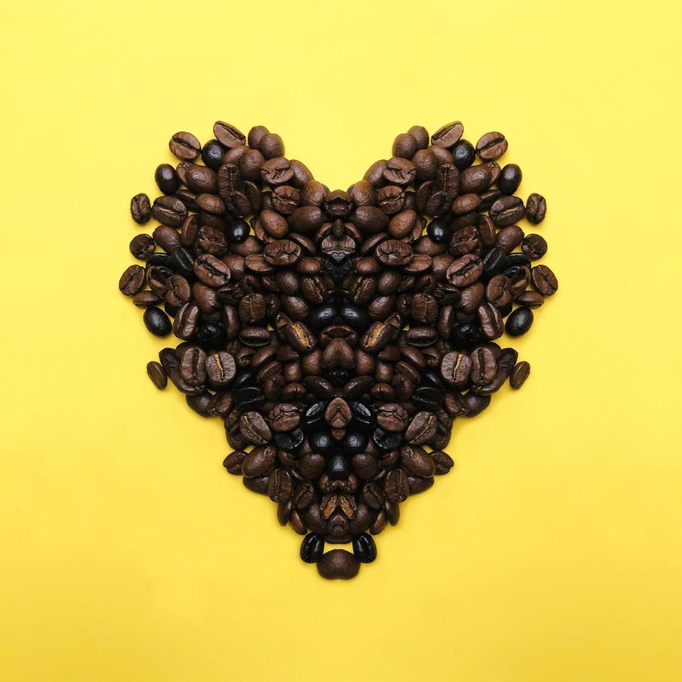 Heart shape roasted coffee beans brown and dark seed variation on yellow background in the center photo