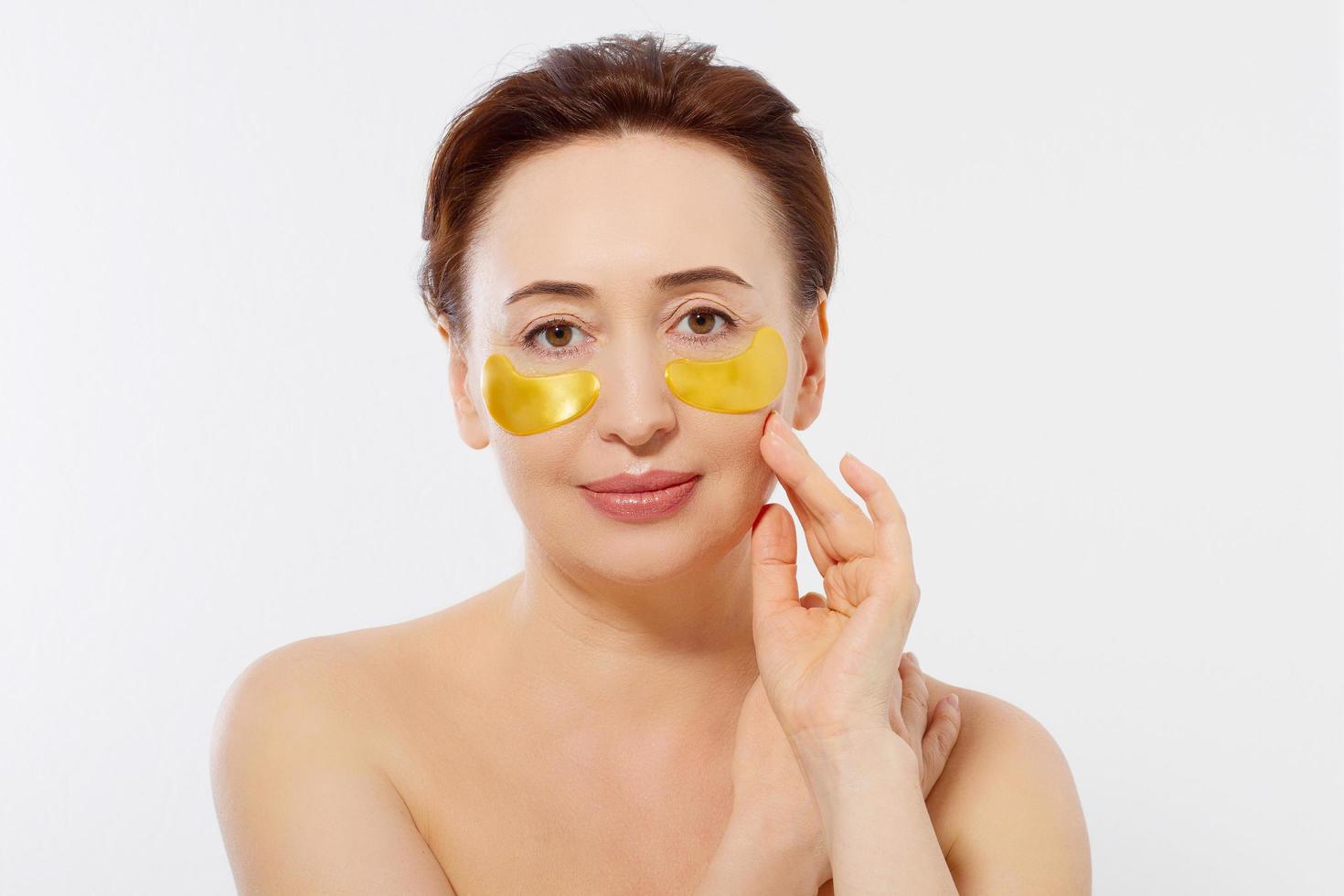 Macro female face. Beauty portrait of middle age woman with wrinkles and a gold patch under eye isolated on white background. Collagen mask and spa concept. Copy space. Summer skin care photo