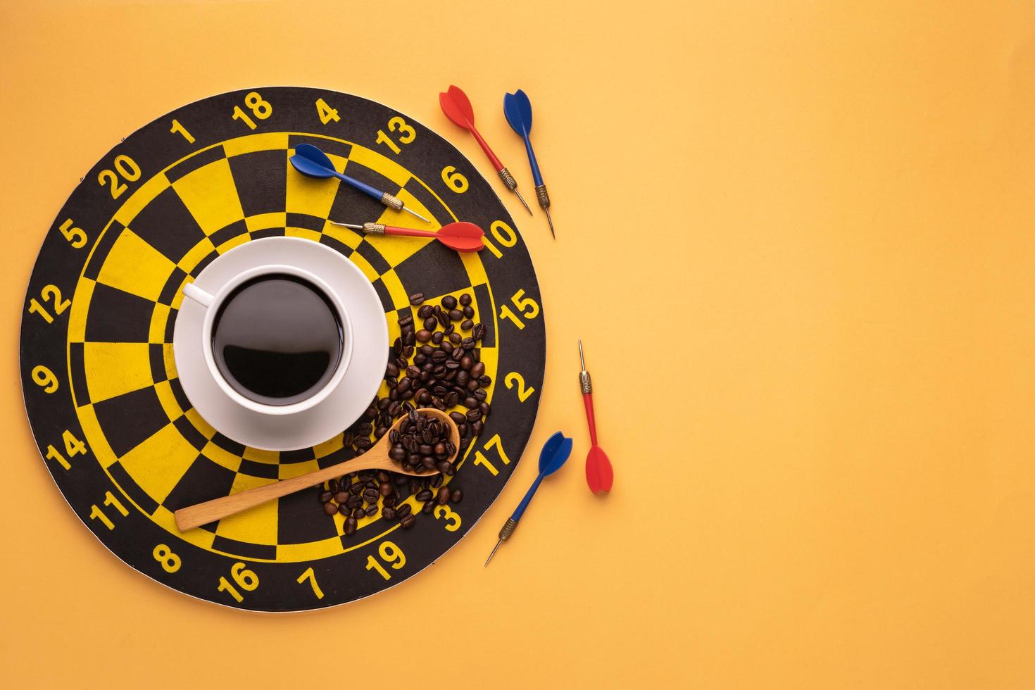 Cup of coffee on dart board on yellow background. Composition with free space for text or design photo