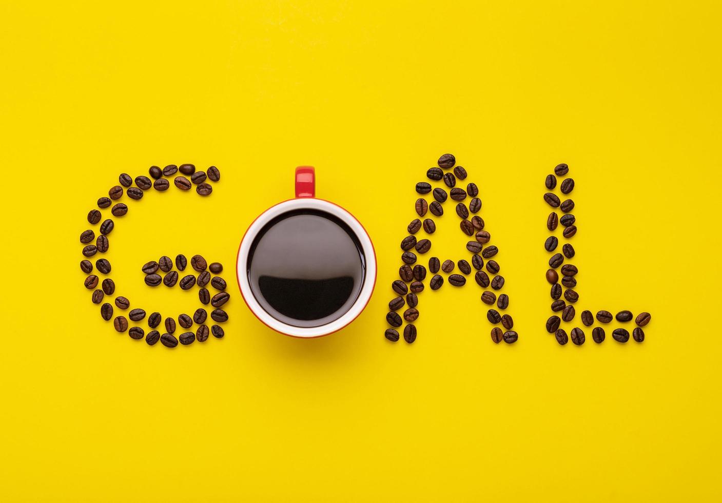Top view Americano in red cup and coffee beans spell for word GOAL on yellow photo