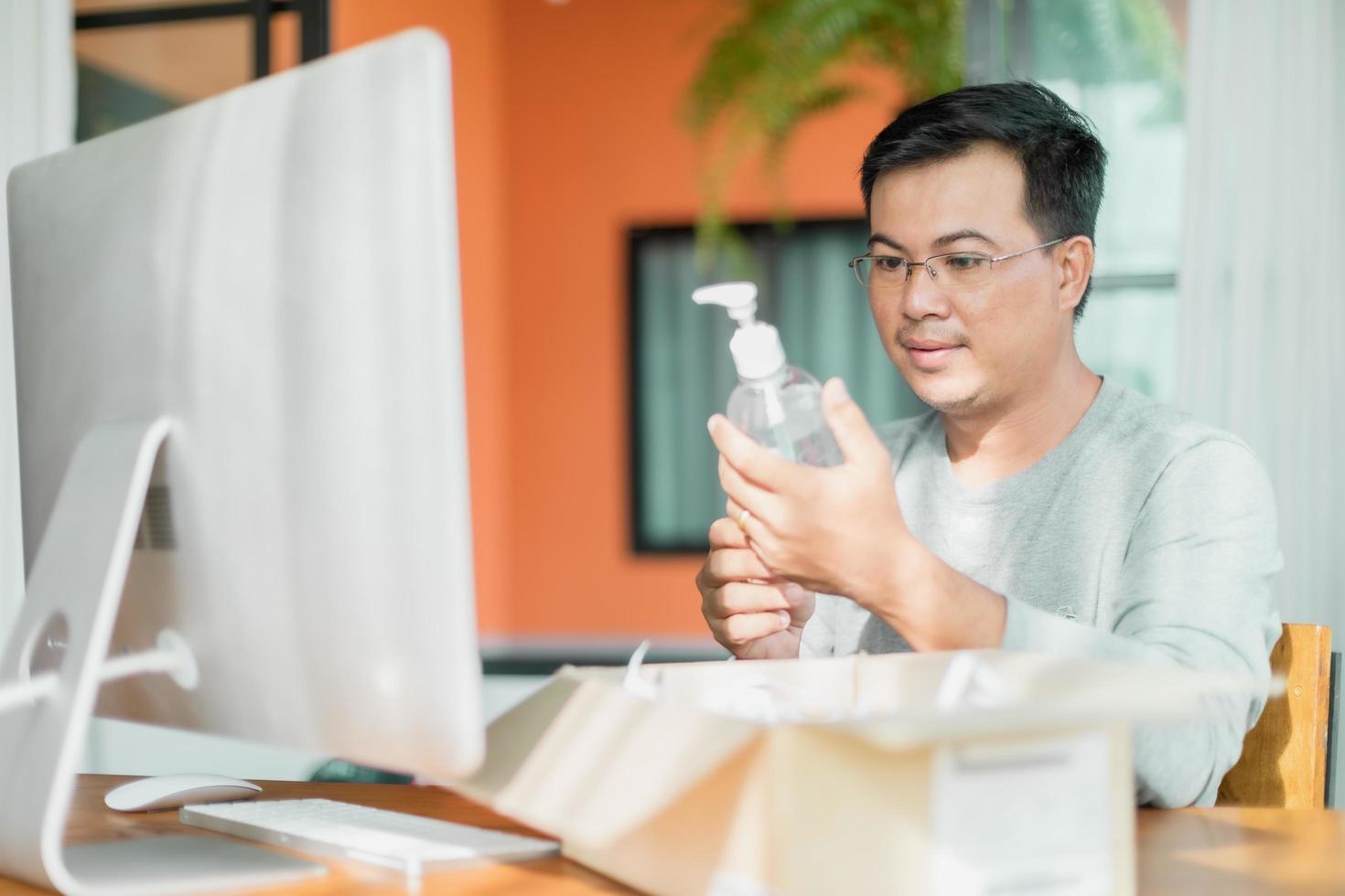 hombre sosteniendo y mirando una botella de gel desinfectante para manos que ordenó usar en casa, trabajo desde casa y concepto saludable foto