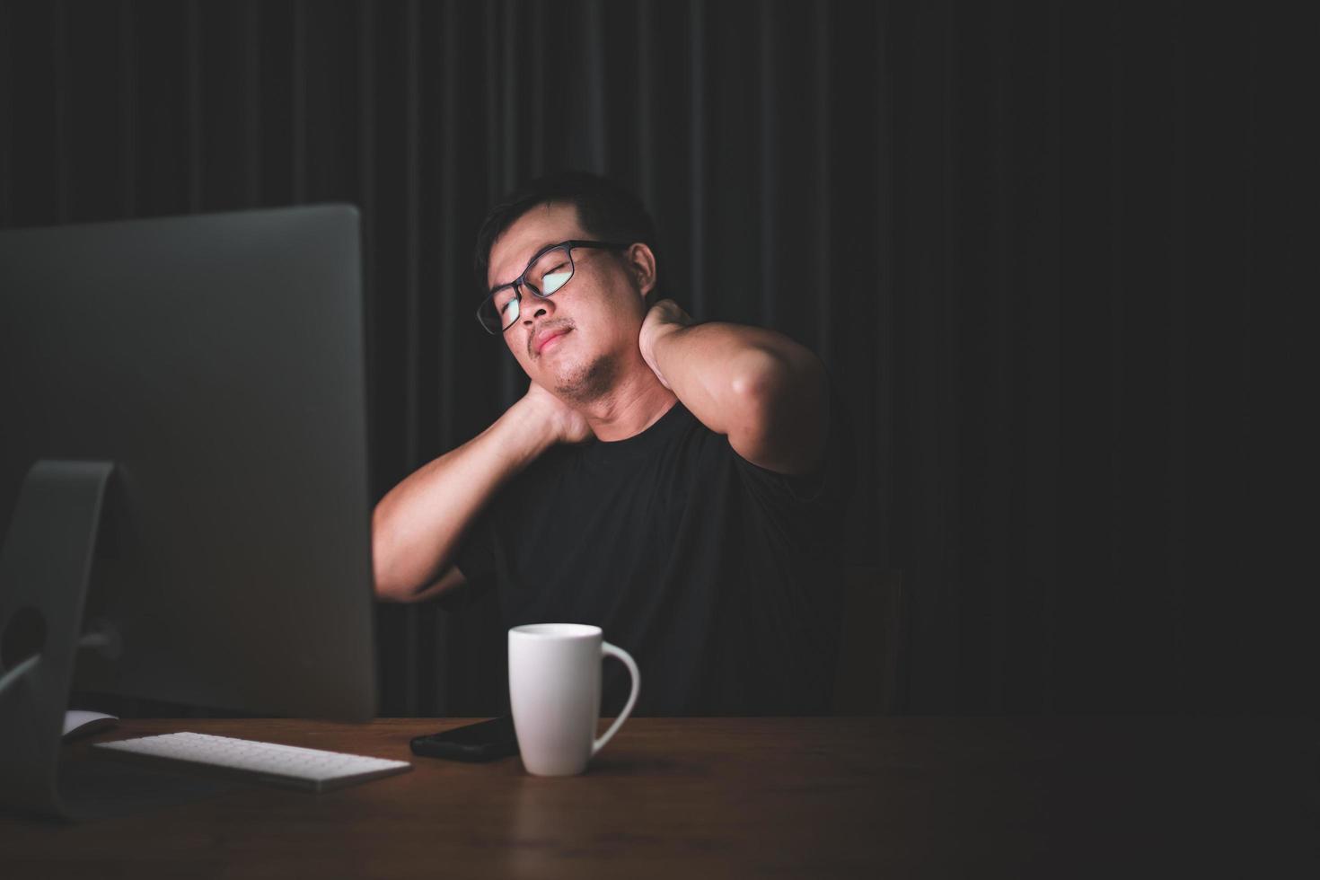 dolor de cuello o concepto cansado. hombre tocándose el cuello porque le duele o duele después de mucho tiempo trabajando en la computadora en la habitación oscura en casa foto