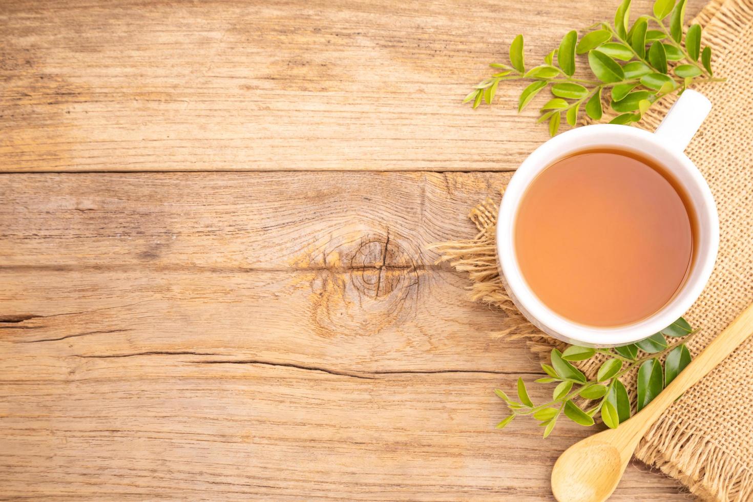 White cup of hot tea and dry tea leaf on wooden table photo