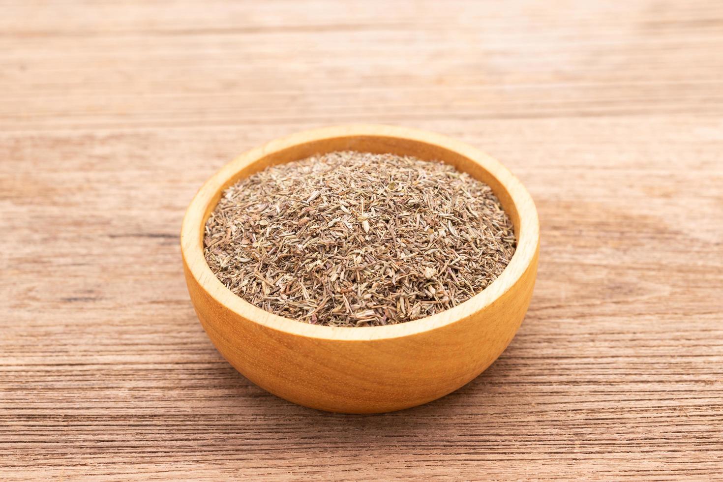 Dry thyme leaves in wooden bowl on wooden plank background. photo