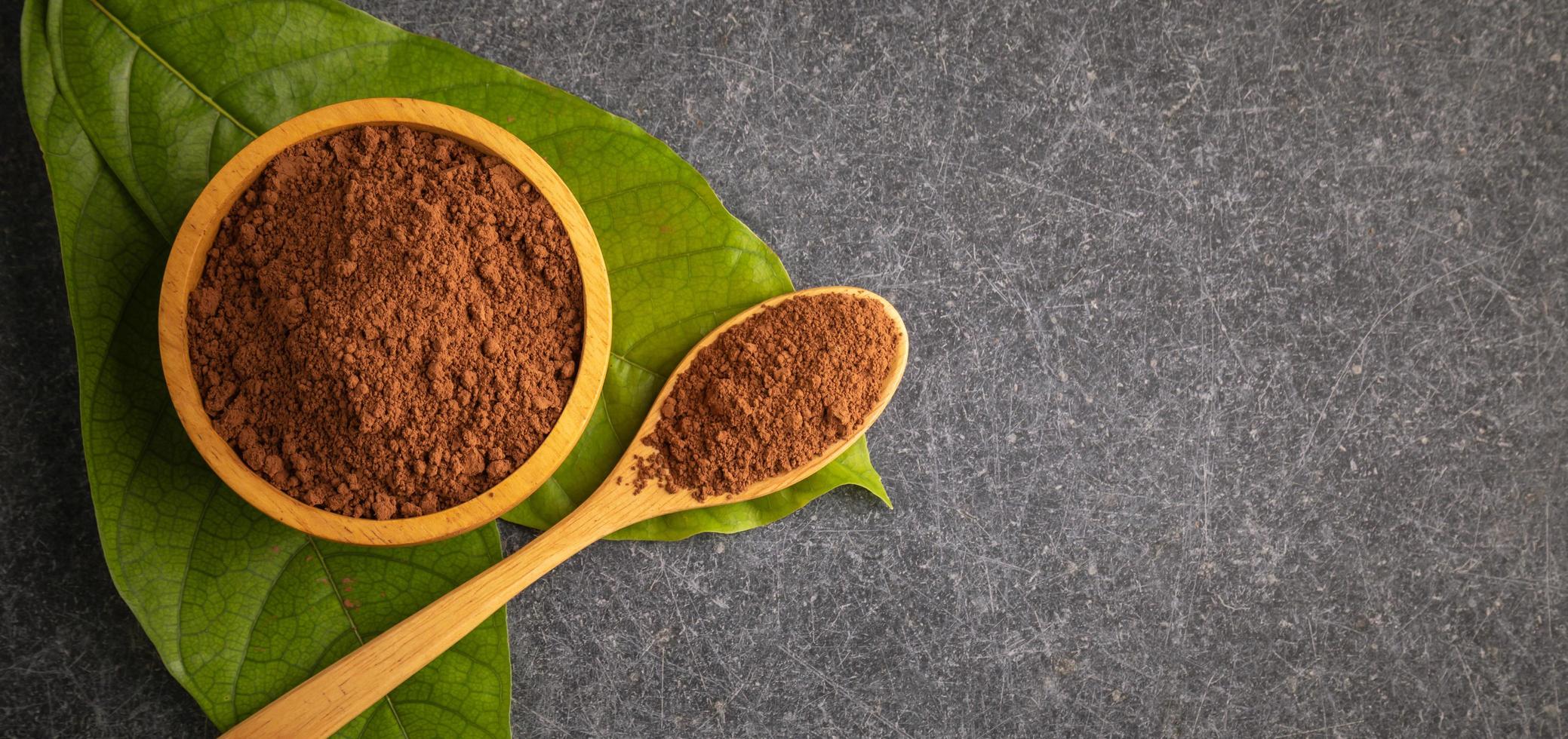 Close up Cocoa powder in wooden bowl and green leaf on stone photo