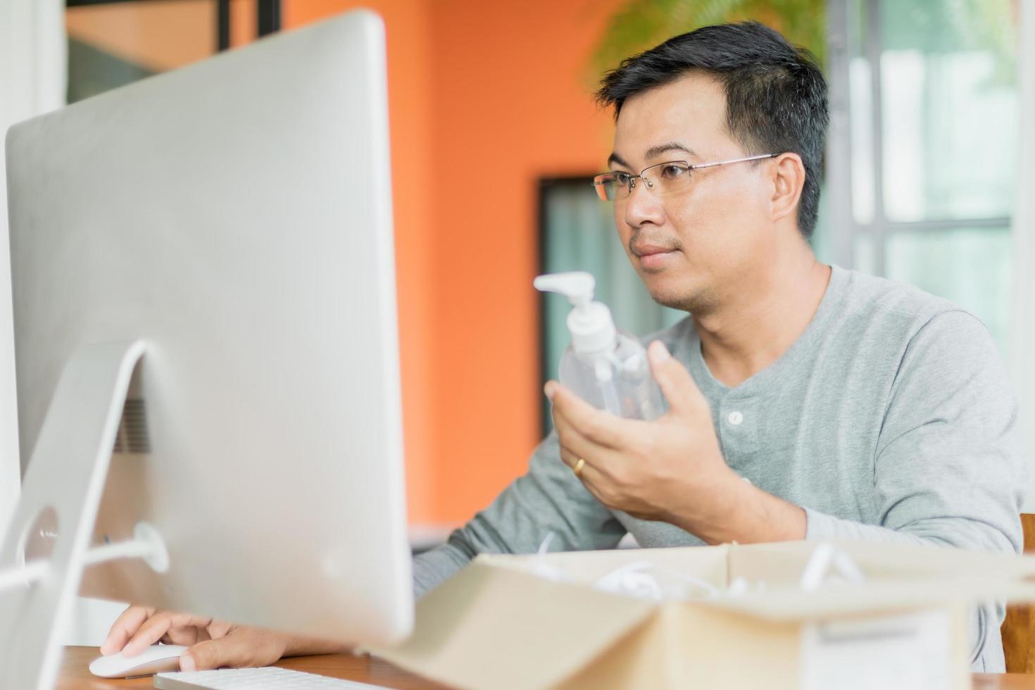 Man holding and looking to hand sanitizer gel bottle that he ordered to use at home, Work from home and Healthy concept photo