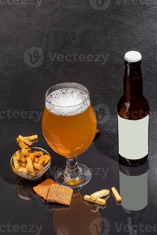 Glasses with different types of craft beer on a wooden bar. In glasses and bottles. Nuts and crackers on the table. On a dark background. photo