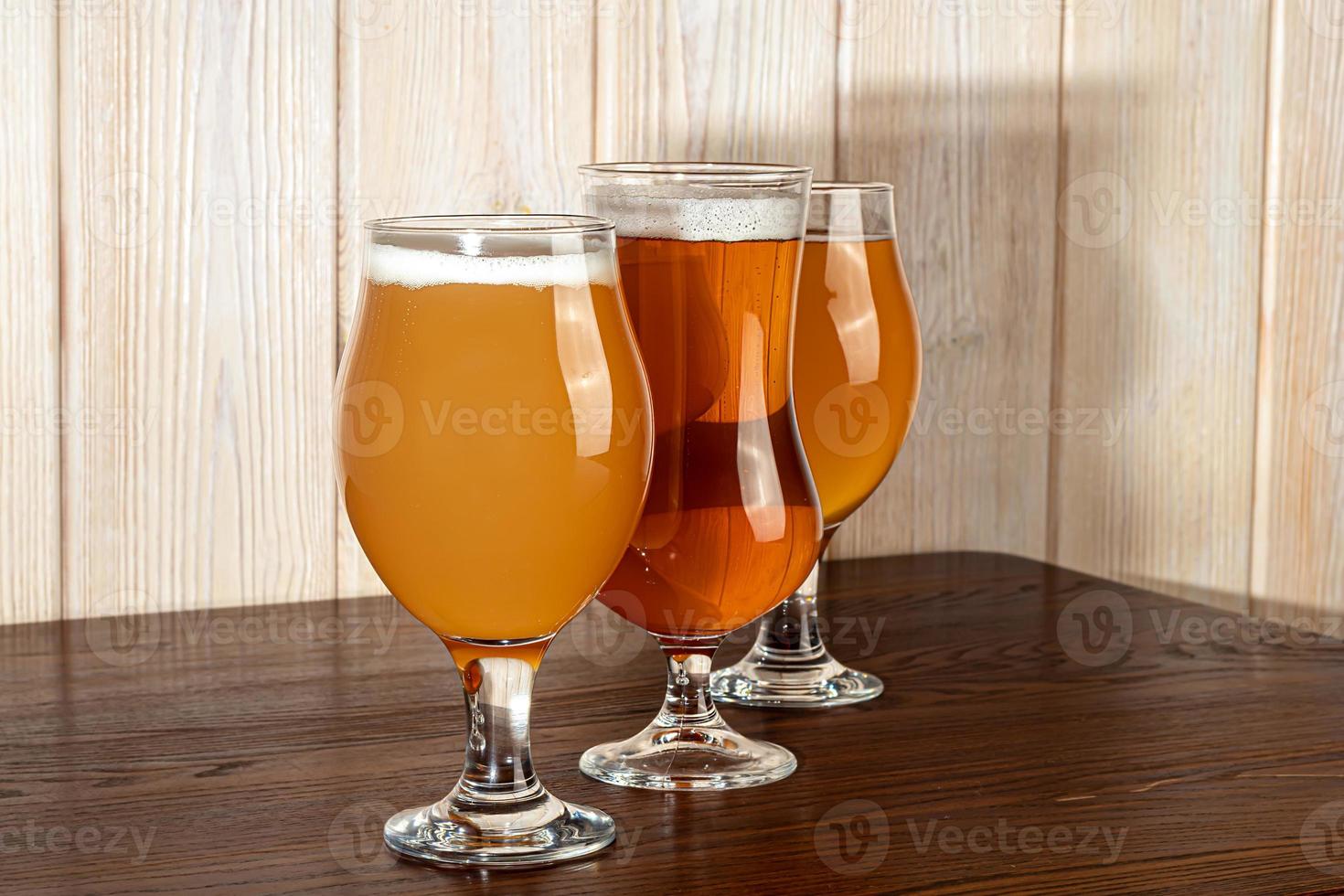 Glasses with different types of craft beer on a wooden bar. In glasses and bottles. Nuts and crackers on the table. On a dark background. photo