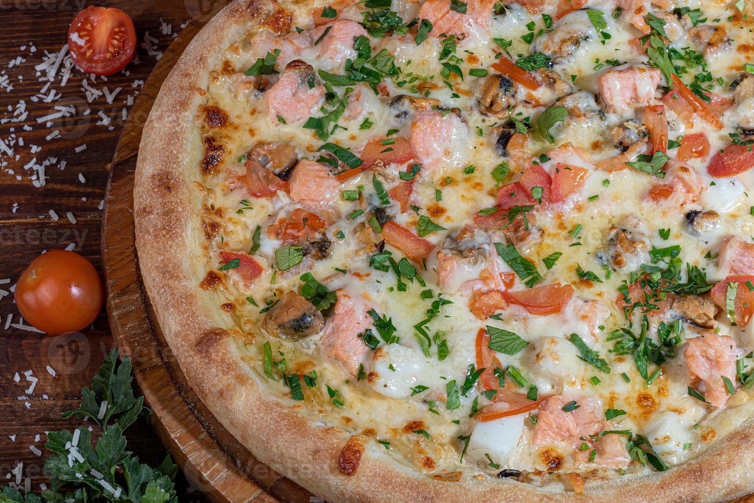 Pizza with bacon and cheese, herbs and cherry tomatoes. With mozzarella, shrimps and octopuses, mussels and other products on a wooden background. photo