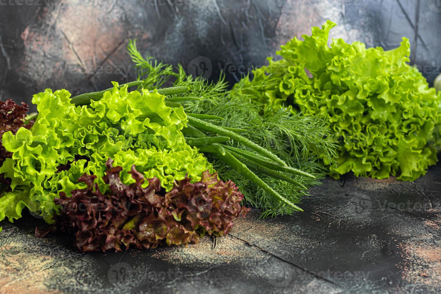 Fresh vegetables for salad. Tomatoes and lettuce, cucumbers with zucchini and cabbage with dill. Spring harvest, benefits and vitamins. On a dark background. photo