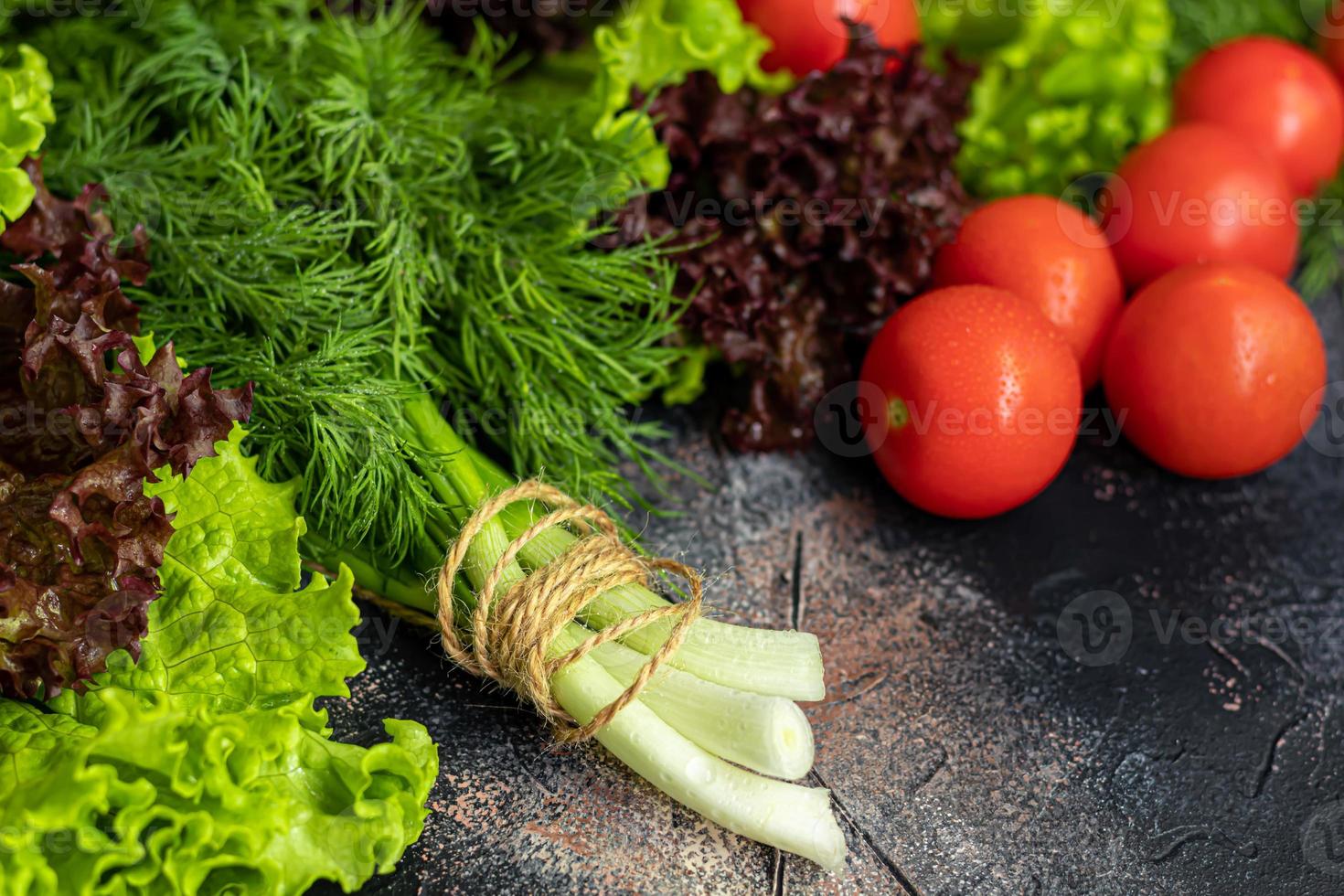 Fresh vegetables for salad. Tomatoes and lettuce, cucumbers with zucchini and cabbage with dill. Spring harvest, benefits and vitamins. On a dark background. photo