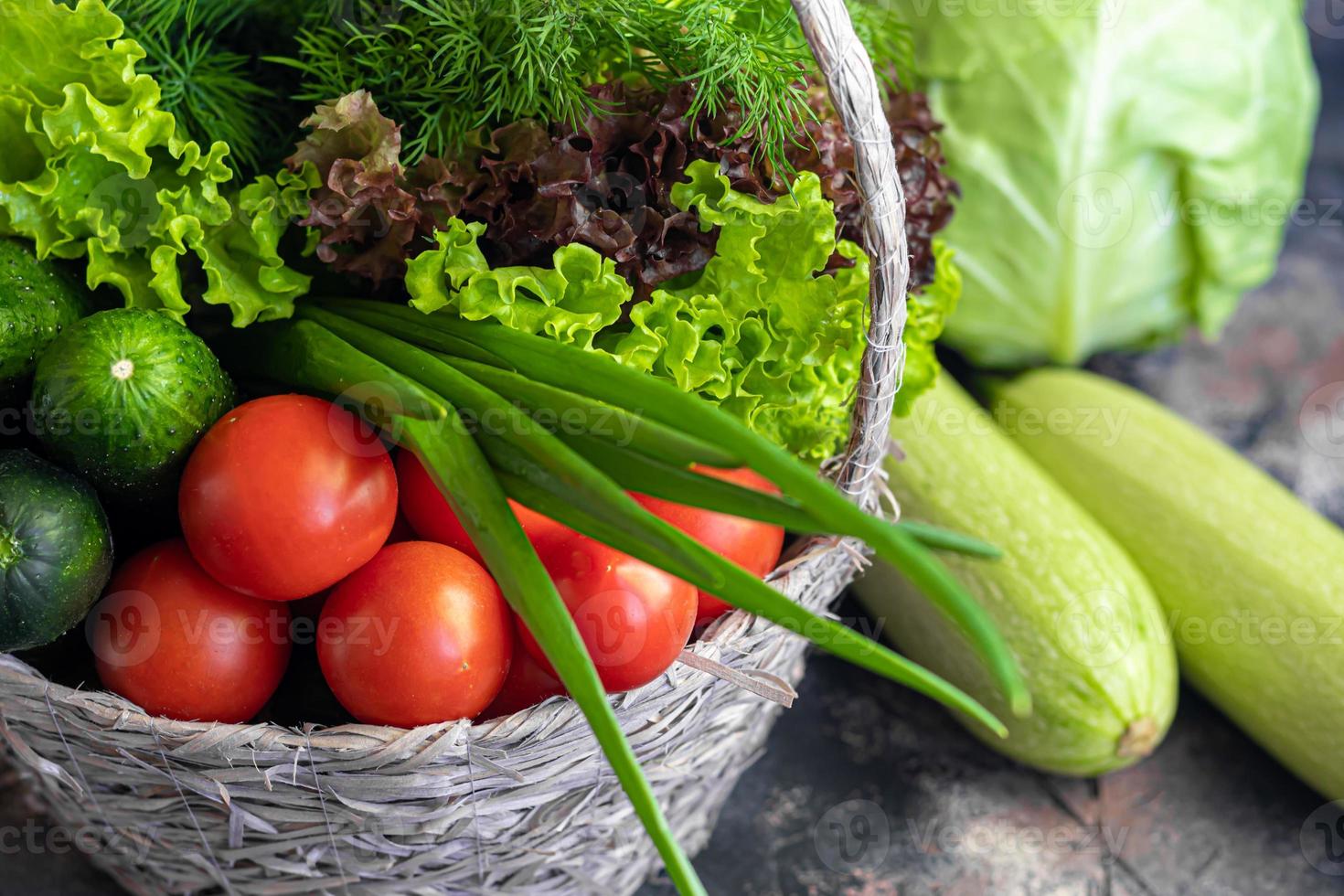 Fresh vegetables for salad in a basket. Tomatoes and cucumbers with zucchini and cabbage with dill. Spring harvest, benefits and vitamins. On a dark background. photo