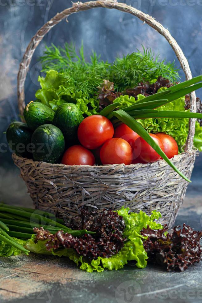 Fresh vegetables for salad in a basket. Tomatoes and cucumbers with zucchini and cabbage with dill. Spring harvest, benefits and vitamins. On a dark background. photo