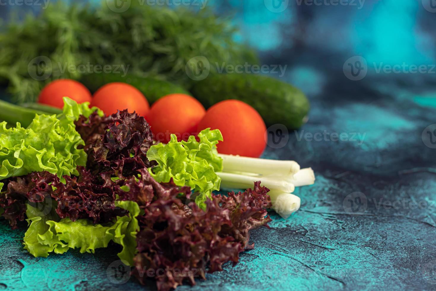 Fresh vegetables for salad. Tomatoes and lettuce, cucumbers with zucchini and cabbage with dill. Spring harvest, benefits and vitamins. On a dark background. photo