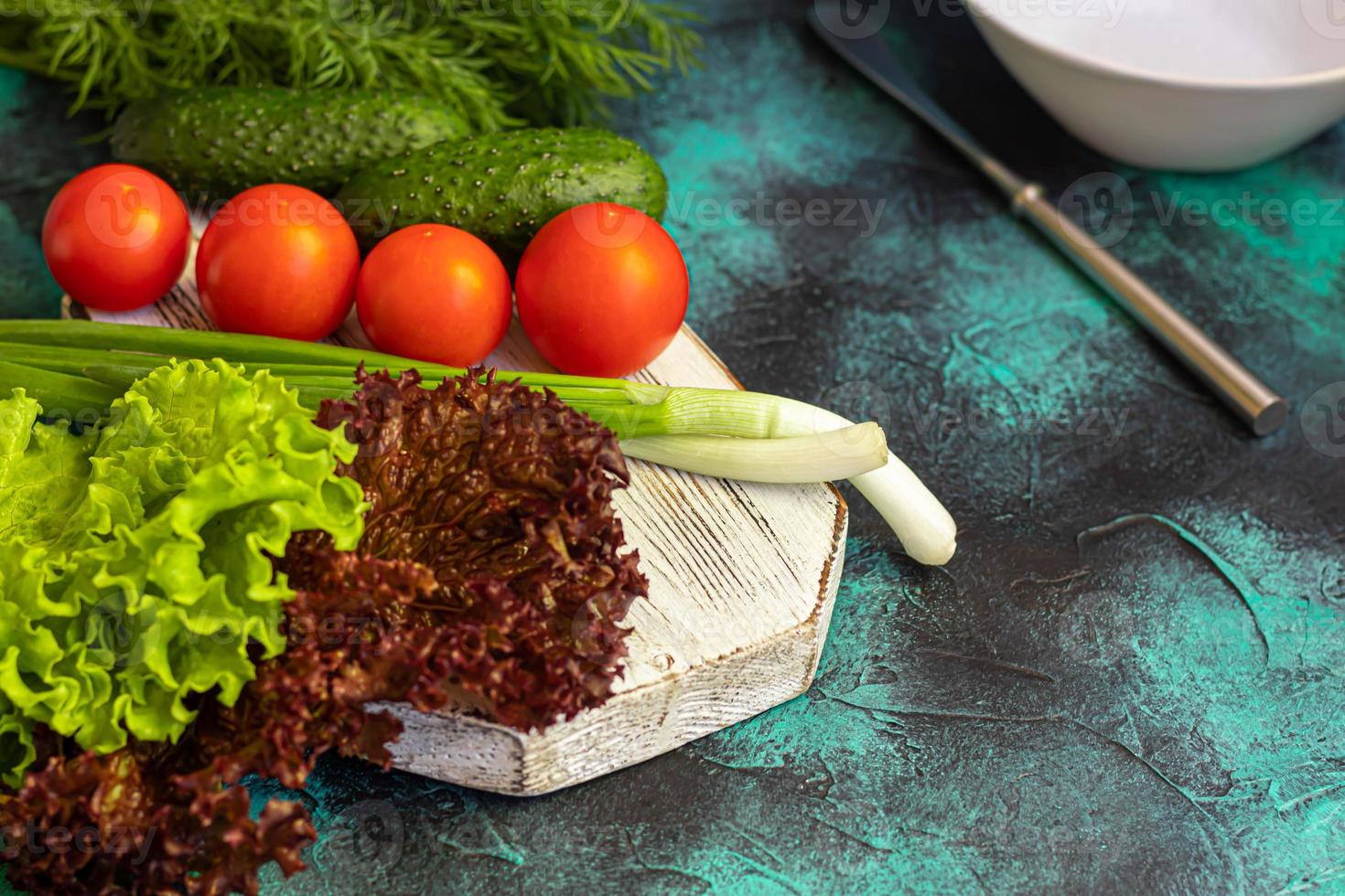 Fresh vegetables for salad. Tomatoes and lettuce, cucumbers with zucchini and cabbage with dill. Spring harvest, benefits and vitamins. On a dark background. photo