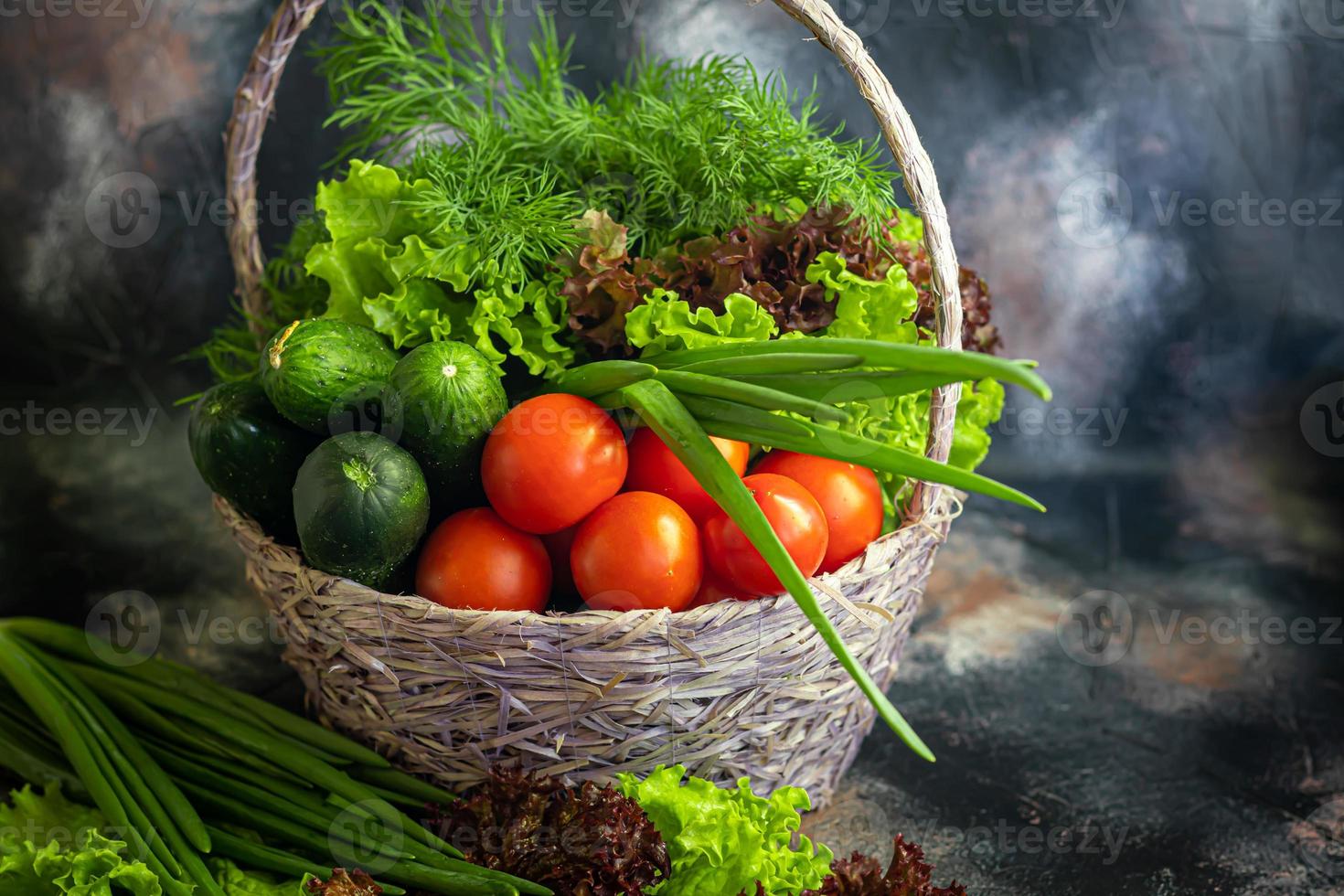 Fresh vegetables for salad in a basket. Tomatoes and cucumbers with zucchini and cabbage with dill. Spring harvest, benefits and vitamins. On a dark background. photo