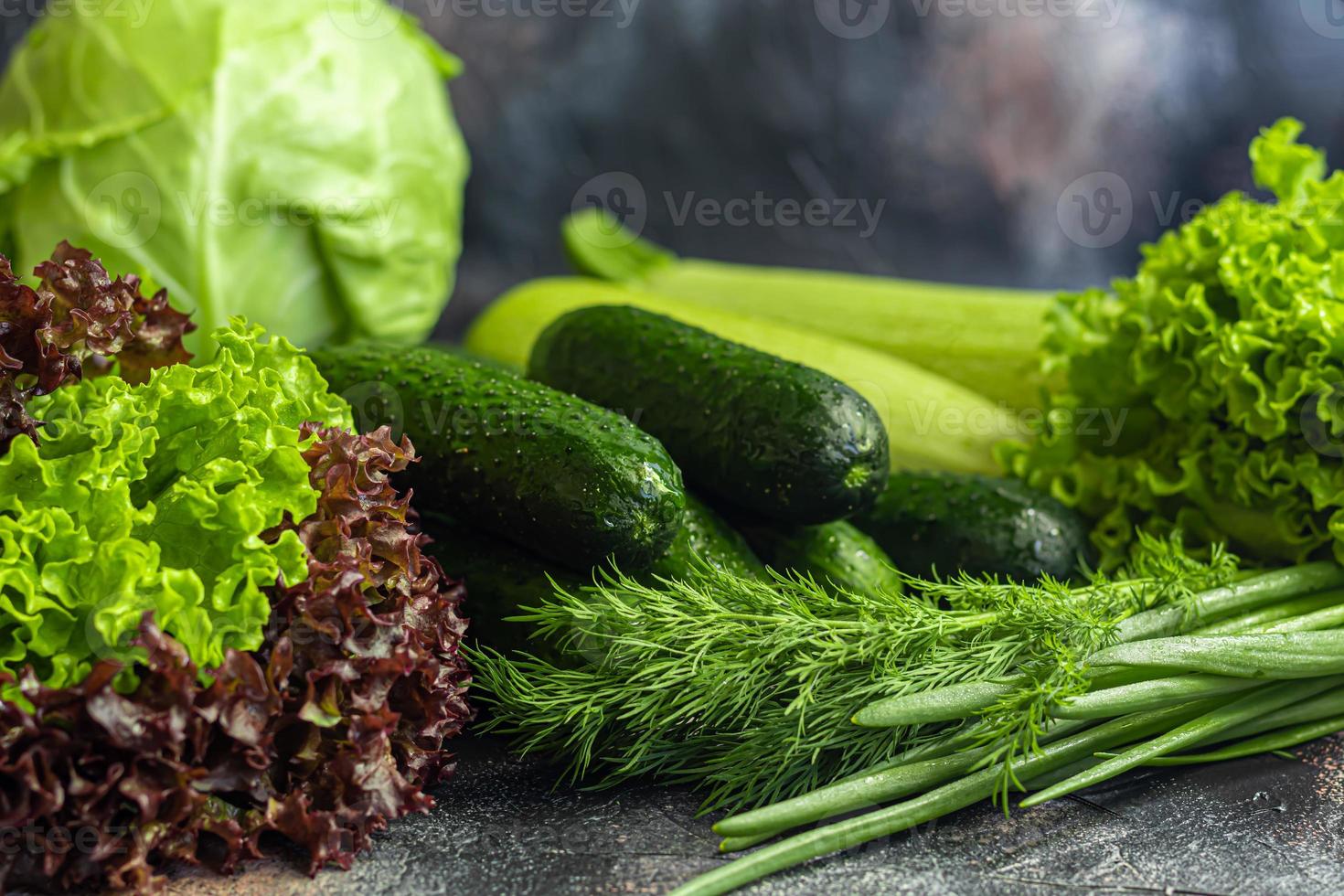 Fresh vegetables for salad. Tomatoes and lettuce, cucumbers with zucchini and cabbage with dill. Spring harvest, benefits and vitamins. On a dark background. photo
