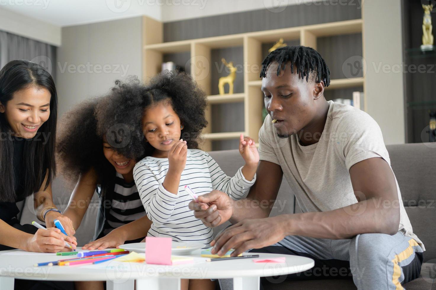 Asian-African American family relaxing, chatting, painting and having fun on vacation in the living room of the house photo