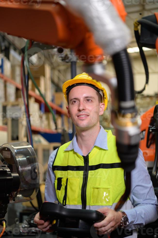 A male worker is controlling a welding robot. by using forcing welding with a control screen which is used for precision welding control. Fast and highly secure photo