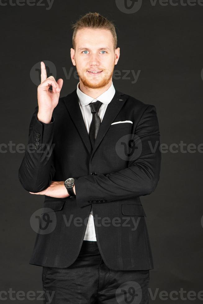 Portrait of young smart and handsome business man in black suit standing on isolated black background. photo