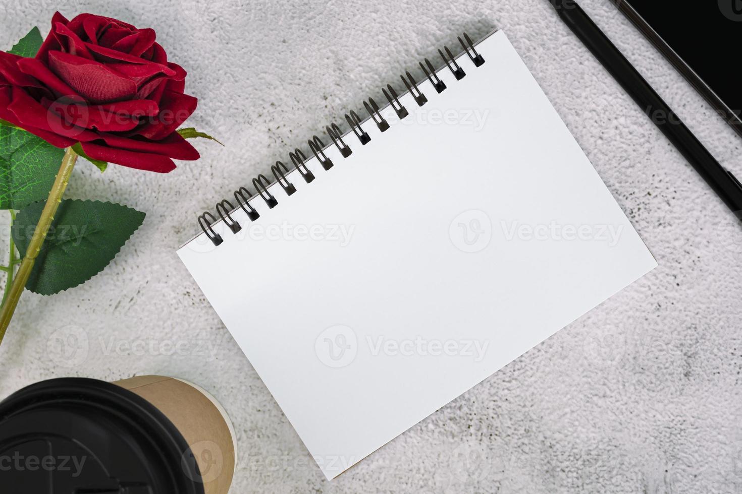 Note book with disposable coffee cup, pen, smartphone and roses on marble table. photo