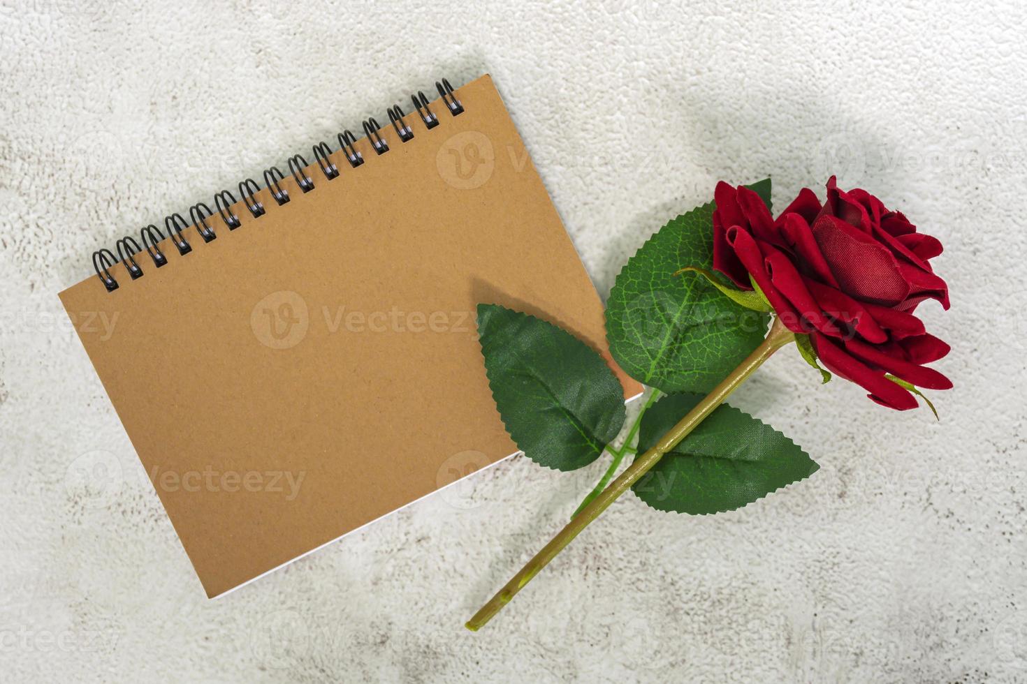 Brown note book with red roses on marble desk. Top view. Flat lay. Copy space. photo